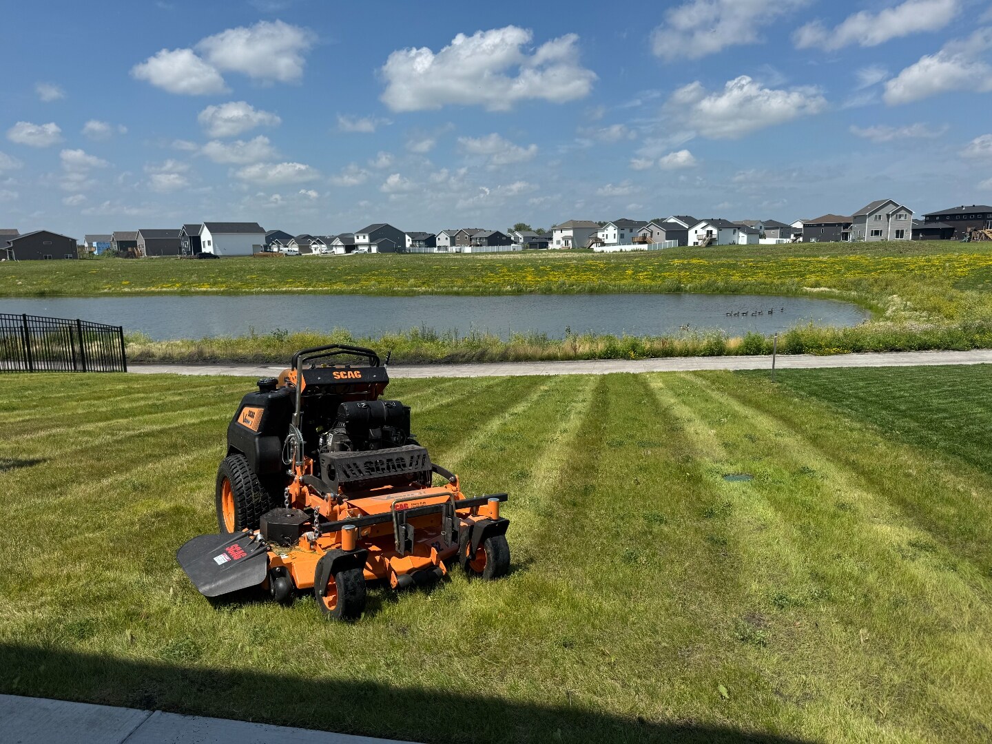 Perfect Turf Scag mower on a freshly striped Fargo-Moorhead lawn near a neighborhood pond