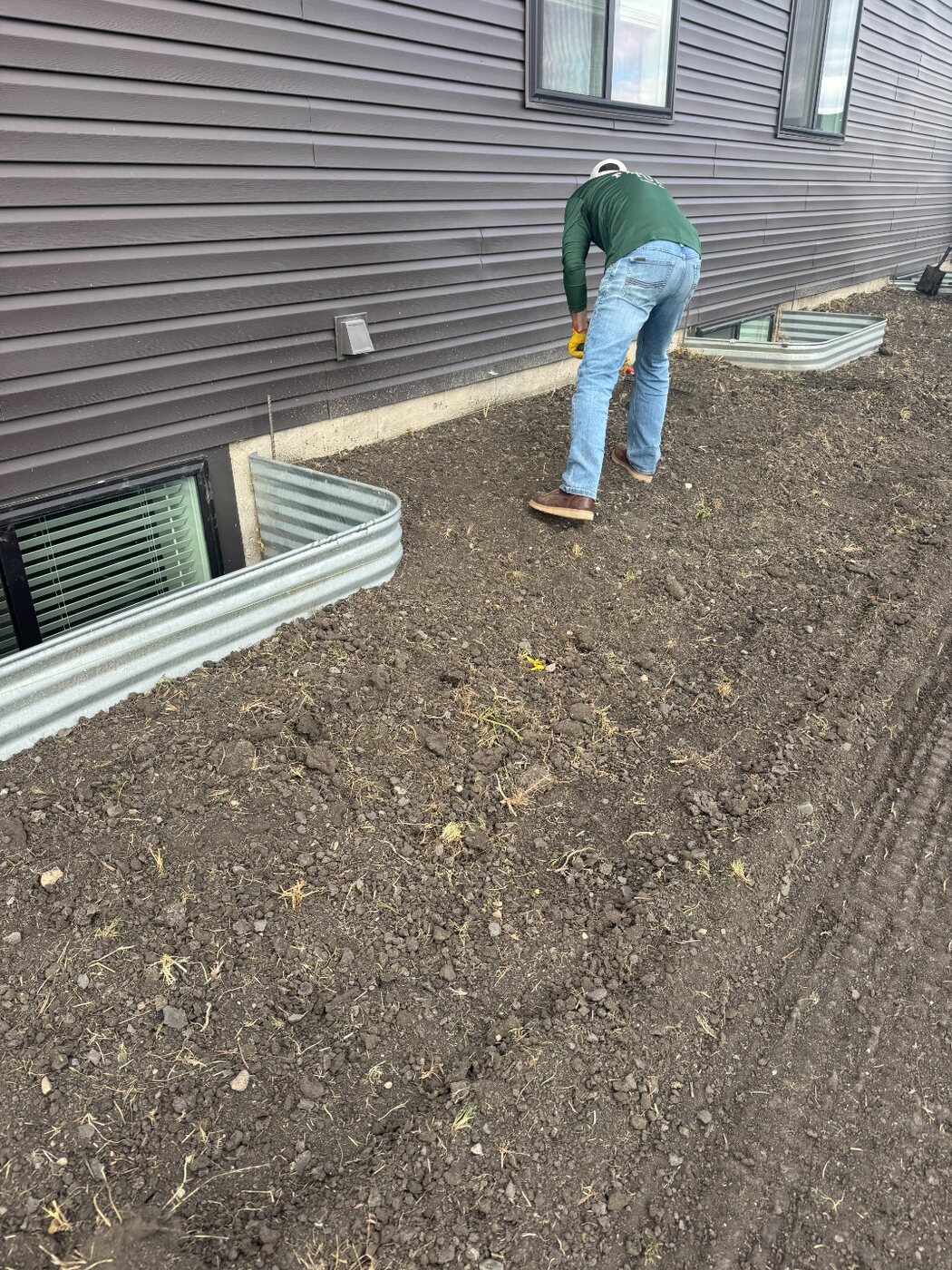 Perfect Turf crew member hand-prepping loose soil along a house foundation before sod installation